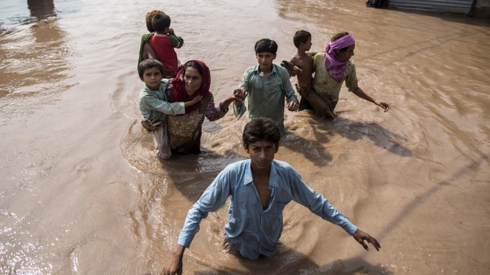 Flood victims wade through a flooded field as they head toward a boat to be evacuated in Jhang