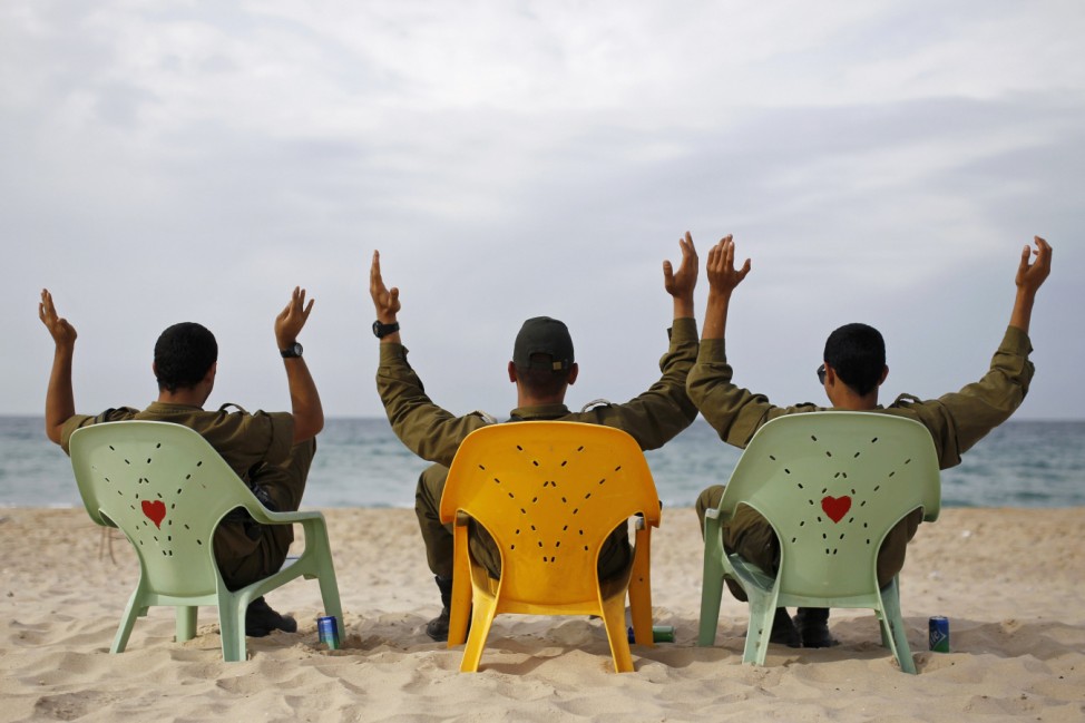 Israeli soldiers gesture as they sit in front of the Mediterranean at Zikim beach near Ashkelon