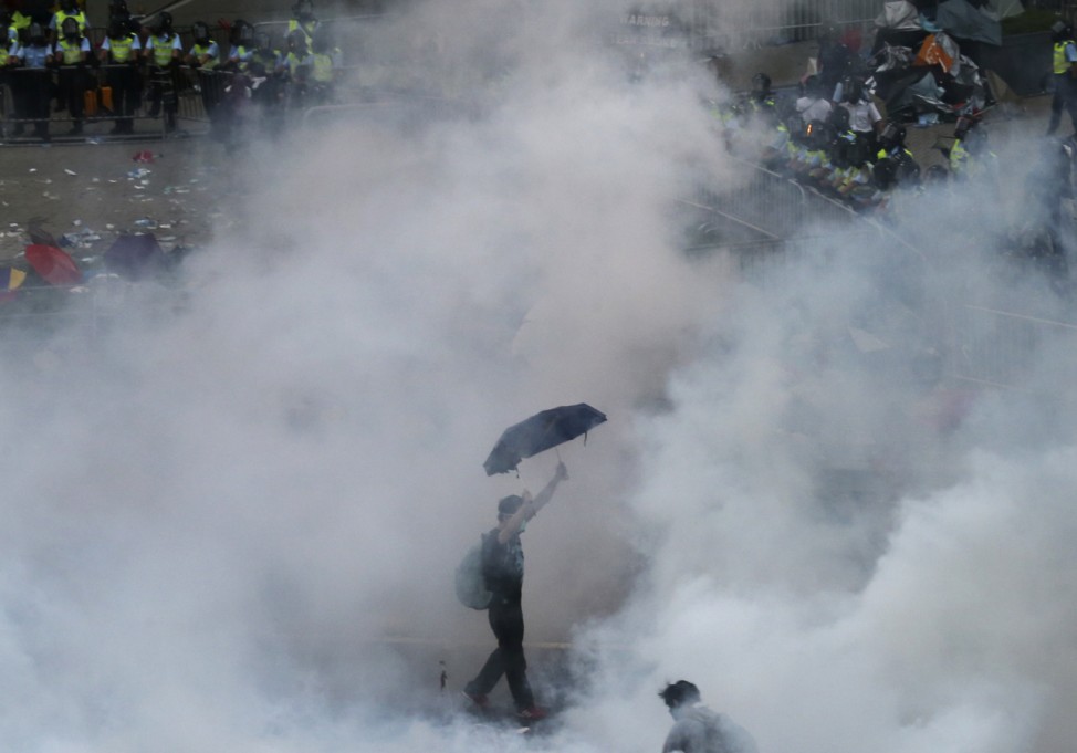 A protester walks in tear gas fired by riot policemen after thousands of protesters blocking the main street to the financial Central district outside the government headquarters in Hong Kong