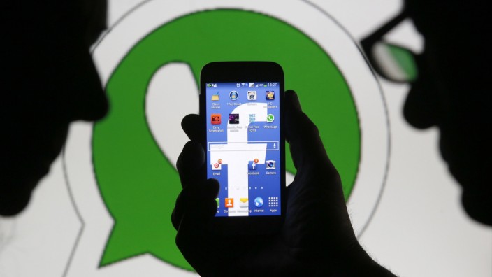 An illustration photo shows a man holding a smart phone with a Facebook logo as its screen wallpaper in front of a WhatsApp messenger logo, in Zenica