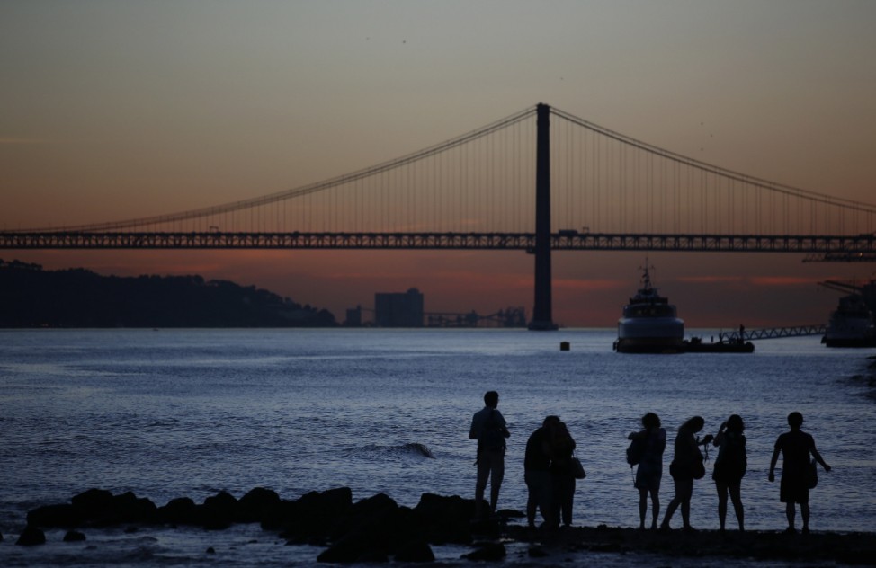 Tourists looks the sunset at the Tagus river near the 25 April bridge in downtown Lisbon