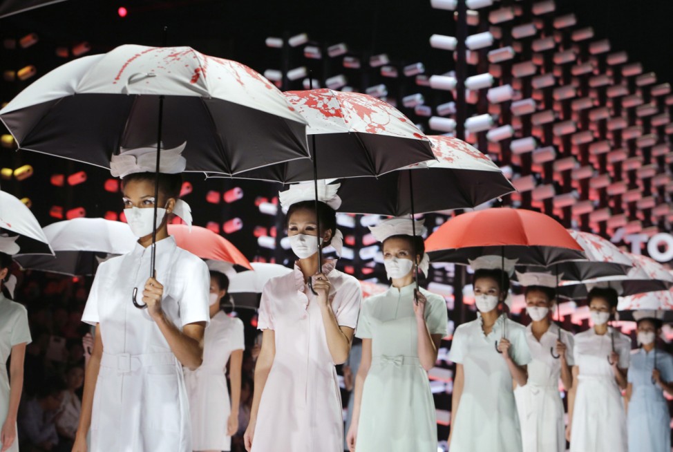 Models wearing masks hold umbrellas as they perform during the TORAY Liu Wei Collection segment at China Fashion Week in Beijing