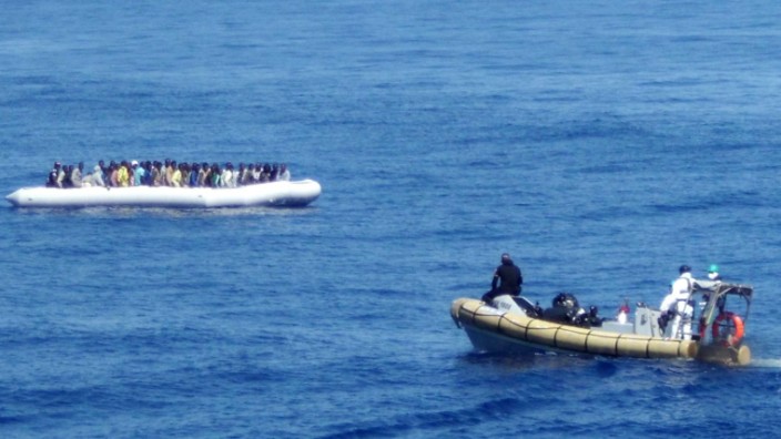 Seenotrettung für Flüchtlinge: Ein Bild der italienischen Marine zeigt eine Rettungsaktion vor der Küste Siziliens - in dem weißen Boot im Hintergrund sind Flüchtlinge zu sehen.
