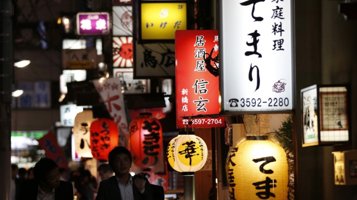 People walk past signboards of restaurants at Tokyo's business district
