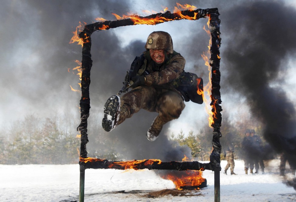 A People's Liberation Army soldier jumps over a burning obstacle during a training session on a snowfield, in Heihe