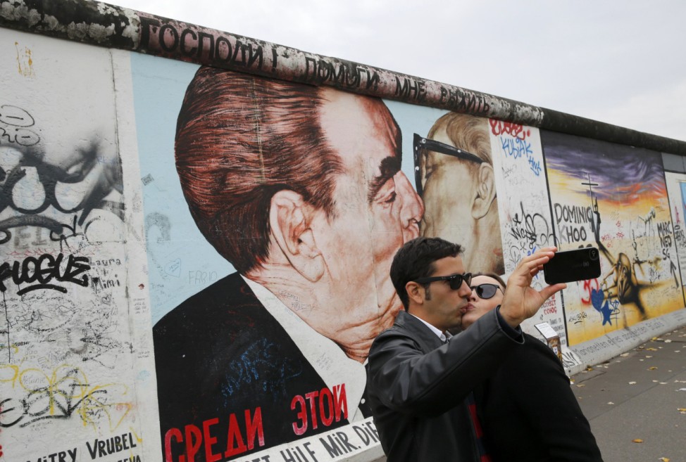 Tourists take pictures with a mobile phone in front of a painting depicting former Soviet leader Brezhnev kissing his East German counterpart Honecker painted on a segment of the former Berlin Wall in Berlin