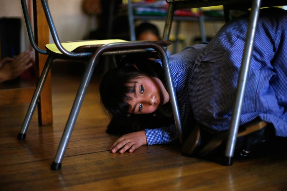 A child takes cover under her school desks inside a school during an earthquake drill in Santiago