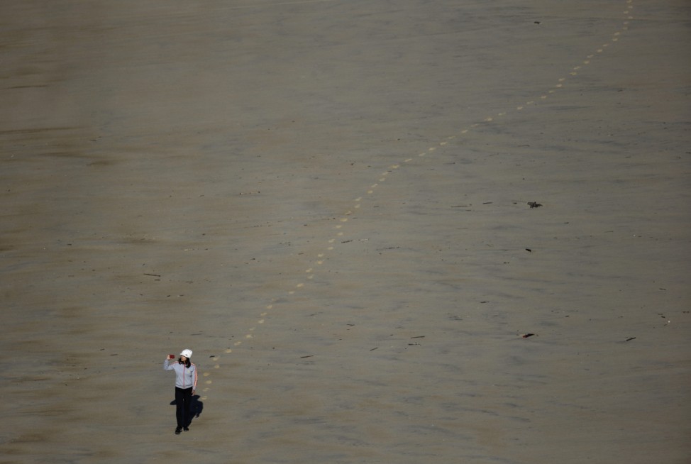 A woman takes photographs as she walks along the Praia do Norte or North beach, in Nazare, Portugal