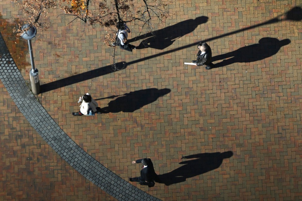 Commuters cast their shadows on the ground as they walk through a park in Tokyo on a winter morning
