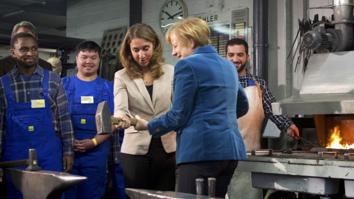 German Chancellor Merkel and German integration officer Oezog lift a smith hammer during their visit of trainees at the public transport company BVG in Berlin