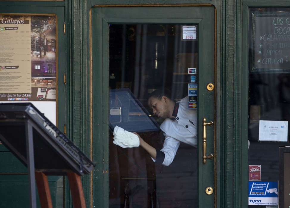 A worker clean the glass of the front door as he prepares to open a restaurant for the day in Madrid, Spain,