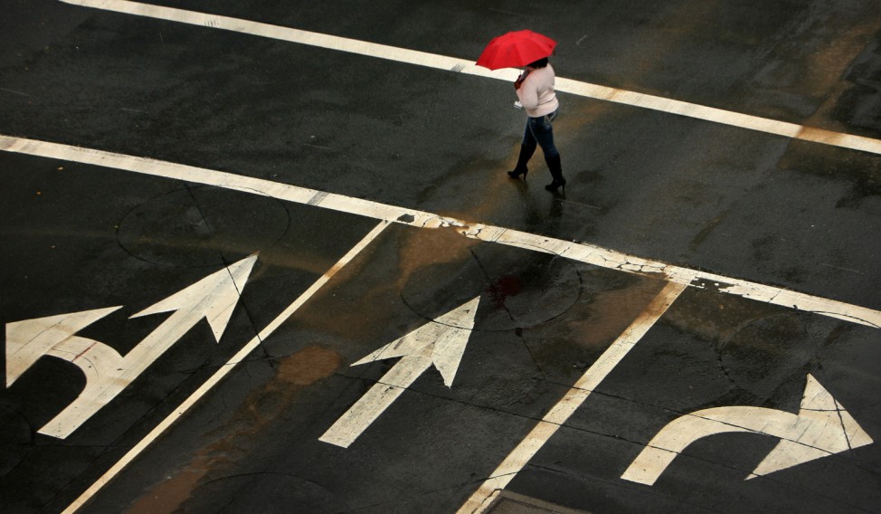 A women, prepared with an umbrella, crosses an intersection in downtown Riverside,