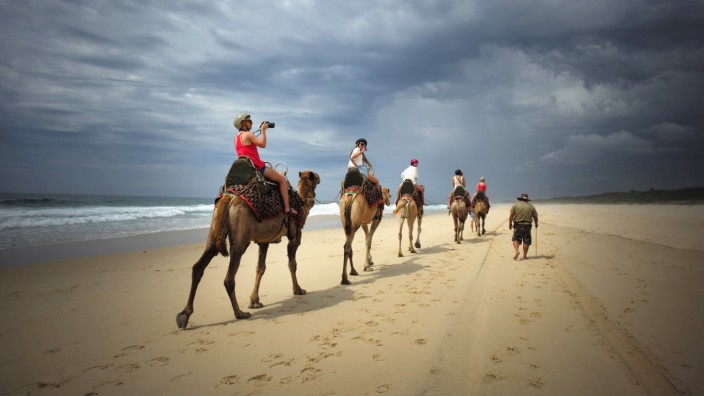 A tourist takes a picture under storm clouds during a camel safari tour alongside the Pacific Ocean on Lighthouse Beach