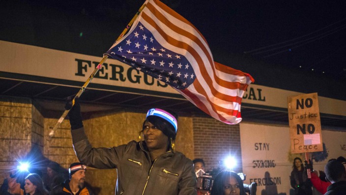 Woman holds an upside-down American flag from a moving vehicle as she takes part in protest near the Ferguson Police Station in Ferguson