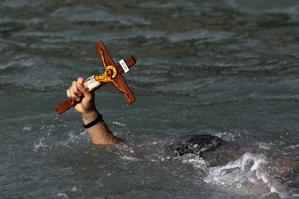 A man holds a cross after a competition to retrieve it from the water during Epiphany day celebrations in the port village of Zygi
