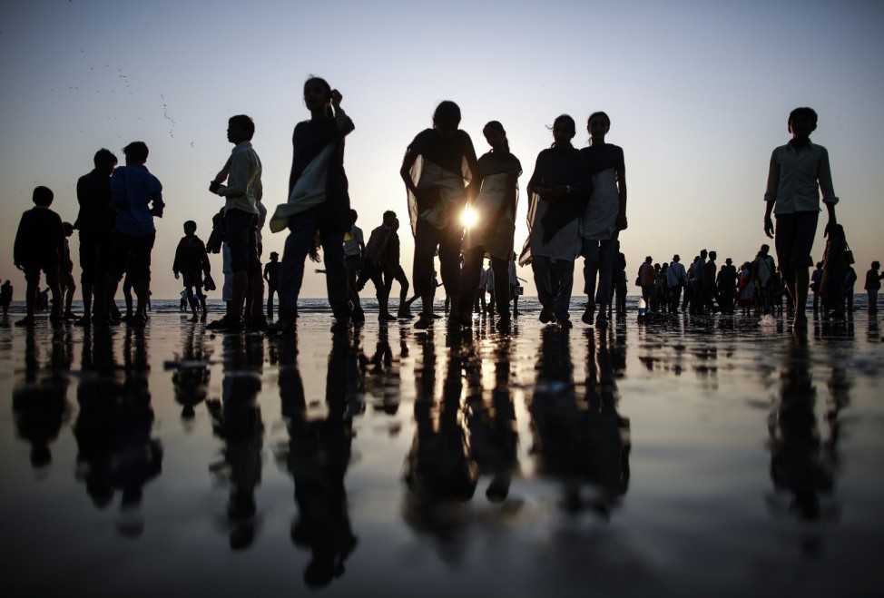 People are silhouetted as they walk on a beach along the shores of the Arabian Sea  in Mumbai