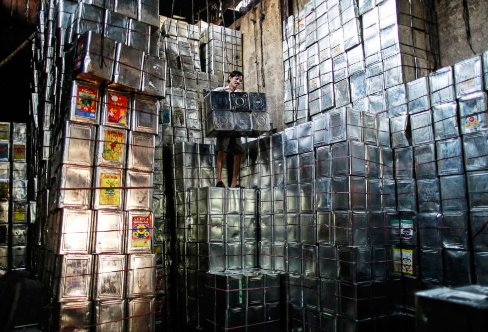 A labourer takes down tin boxes inside a tin container recycling factory in a slum area in Mumbai