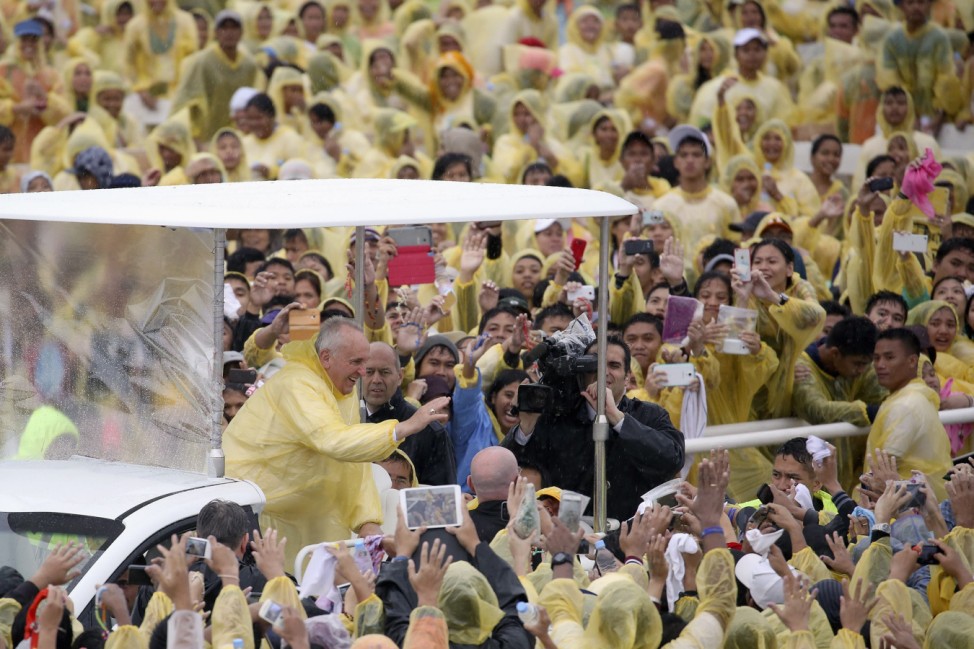Pope Francis, wearing a yellow raincoat, waves to pilgrims after holding a mass at Tacloban's airport