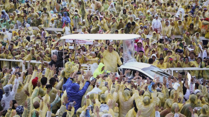 Pope Francis, wearing a yellow raincoat, waves to pilgrims after holding a mass at Tacloban's airport