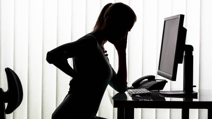 Silhouette of woman at desk having back pain model released Symbolfoto PUBLICATIONxINxGERxSUIxAUTxHU