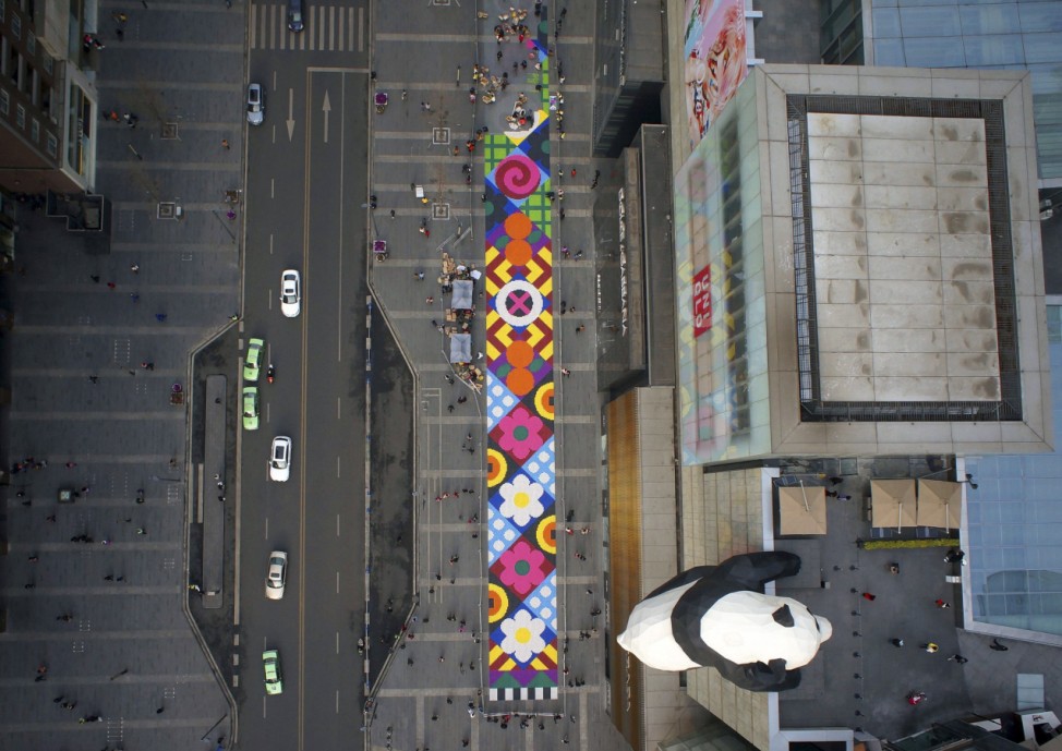 Giant 'carpet' with candies on a pedestrian street next to a panda sculpture hanging on the exterior wall of a department store, in Chengdu