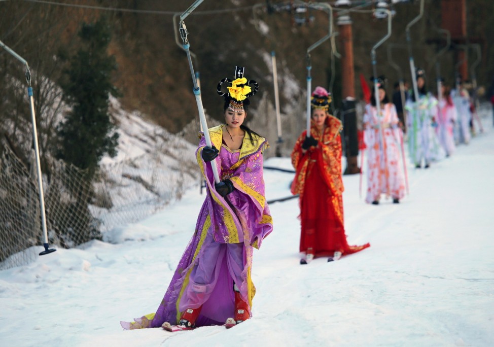 Women dressed in Chinese traditional costumes hold onto a ski lift as they are transferred to top of a ski trail during a promotional event at a ski resort in Sanmenxia