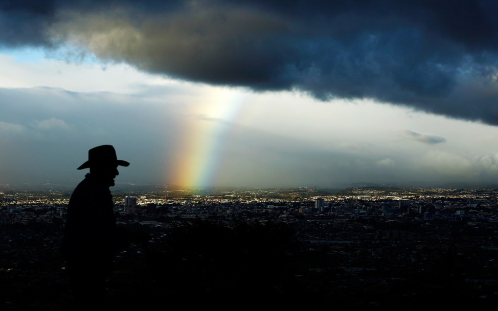 Man walks as a rainbow is seen below dark clouds in San Jose city