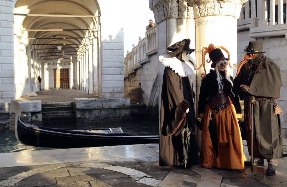 Masked revellers pose near a canal next to St. Mark's square during the first day of carnival, in Venice