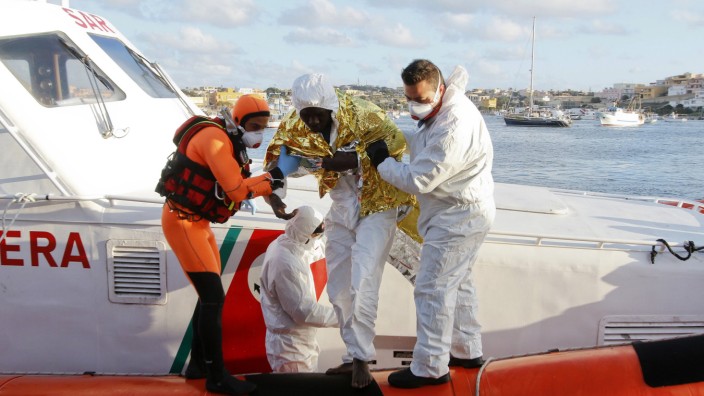 A migrant who survived a shipwreck is helped as he arrives with others at the Lampedusa harbour
