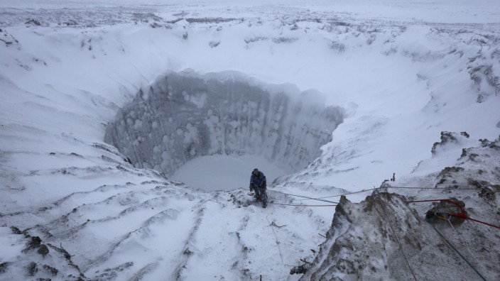 A member of an expedition group stands on the edge of a newly formed crater on the Yamal Peninsula, northern Siberia