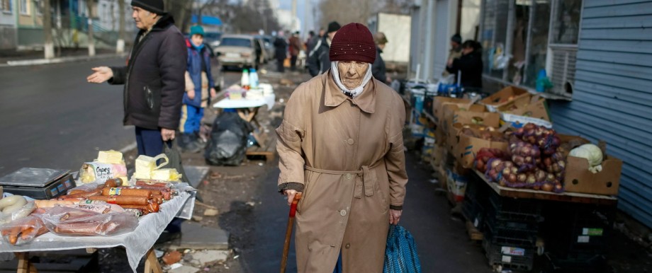A woman walks past street vendors at a residential sector affected by shelling in Mariupol, a city on the Sea of Azov, eastern Ukraine