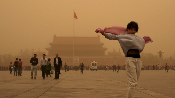 A tourist gestures as she poses for a photograph at Tiananmen Square during a sandstorm in Beijing