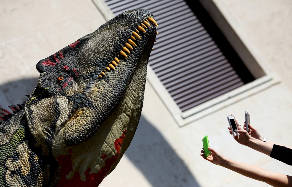 People take pictures with their mobile phone of a scale model of a dinosaur displayed in front of La Sapienza University headquarters in Rome; Dinosaurs