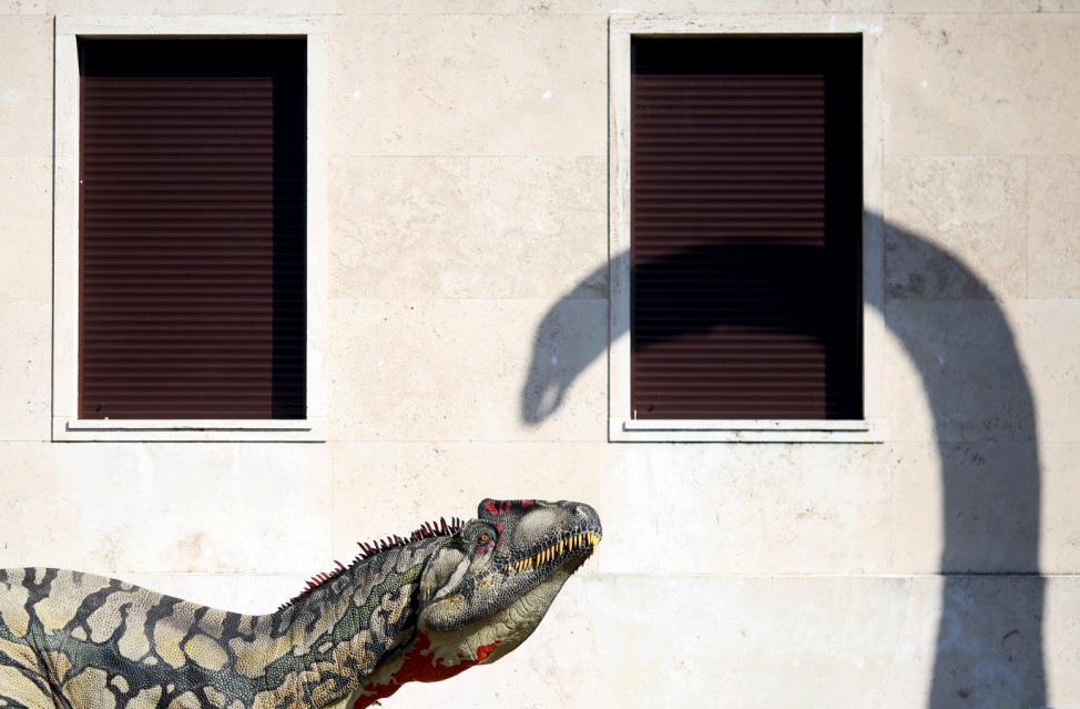 A scale model of a dinosaur and a shadow of another are seen displayed in front of La Sapienza University headquarter in Rome; Dinosaurs