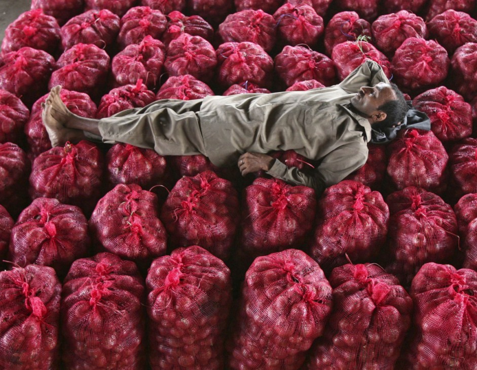 A man takes a nap on sacks filled with onions at a wholesale vegetable market on the outskirts of Jammu