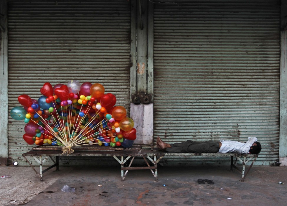 A balloon seller takes a nap in front of the closed shops on the occasion of Eid-al-Fitr in Delhi