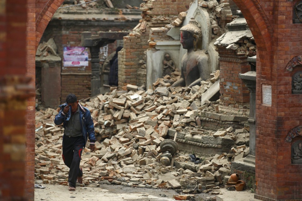 Man cries as he walks on the street while passing through a damaged statue of Lord Buddha a day after an earthquake in Bhaktapur
