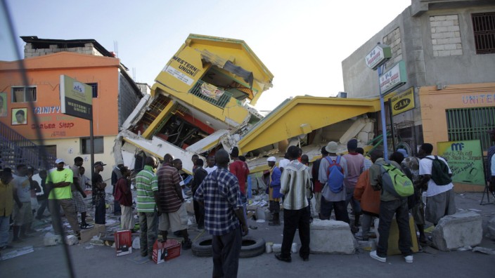 People look at a destroyed building in Port-au-Prince