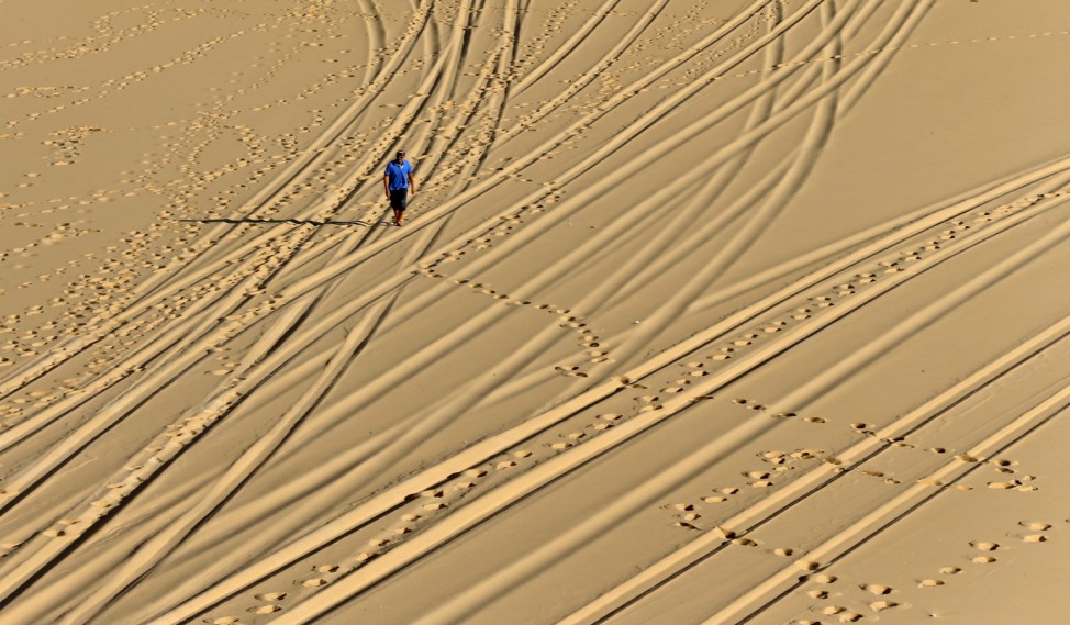 A man walks near tracks in the sands created by four-by-four vehicles in the White Desert north of the Farafra Oasis southwest of Cairo