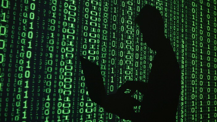 File illustration of a projection of binary code around the shadow of a man holding a laptop computer in an office in Warsaw