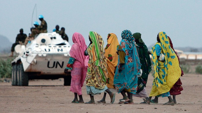 Displaced Sudanese women walk past an armoured personnel carrier (APC) of United Nations-African Union Mission in Nyala, southern Darfur