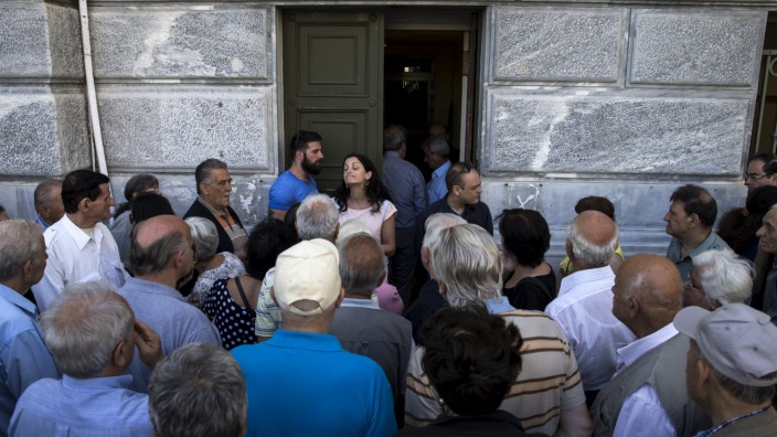 People, most of them pensioners, argue with a staff member outside a closed National Bank branch at the bank's headquarters in Athens