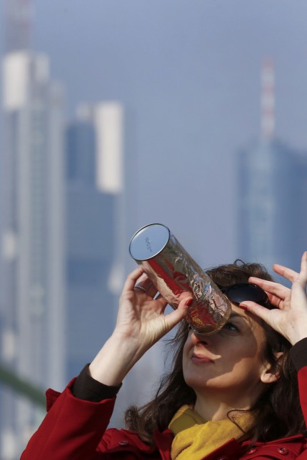 Simic uses a self-made monocular to watch a partial solar eclipse on the bank of river Main in front of the skyline of Frankfurt