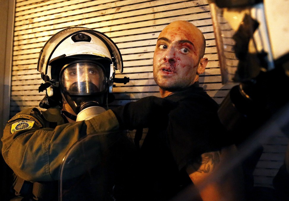 A protester bleeds as he is arrested by riot police following clashes in Athens