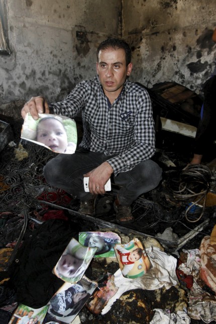 Relative of 18-month-old Palestinian baby Ali Dawabsheh, who was killed after his family's house was set to fire in a suspected attack by Jewish extremists, shows his picture at the burnt house in Duma village near the West Bank city of Nablus