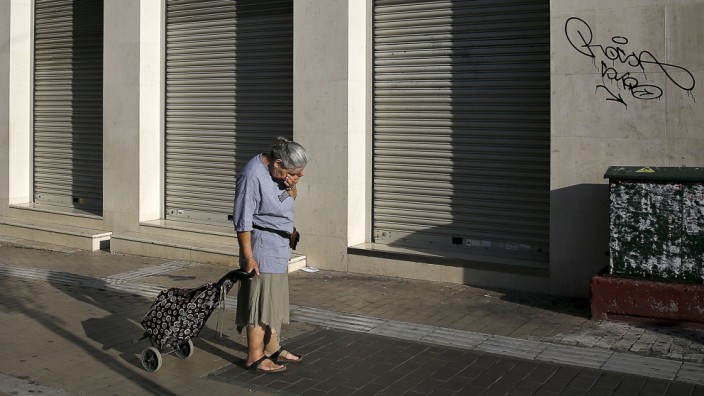 A woman pulling a shopping cart reacts outside a closed Eurobank branch in Athens
