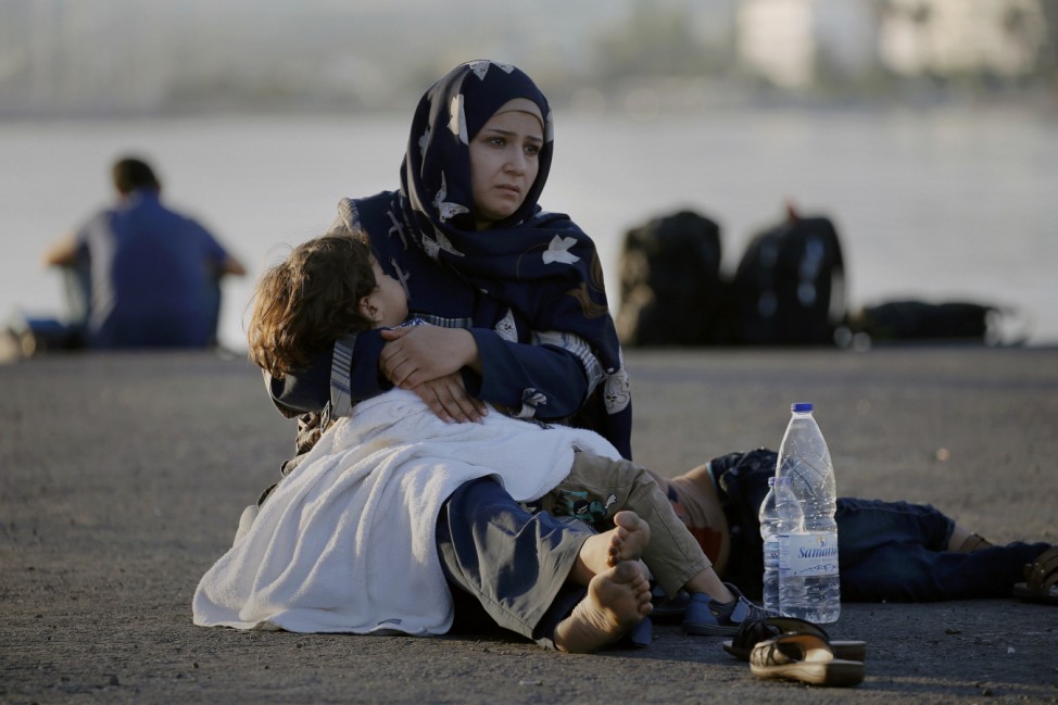 A Syrian refugee holds his child in her arms as she sits in the port of the Greek island of Kos waiting to be registered and move with her family to the 'Eleftherios Venizelos' vessel