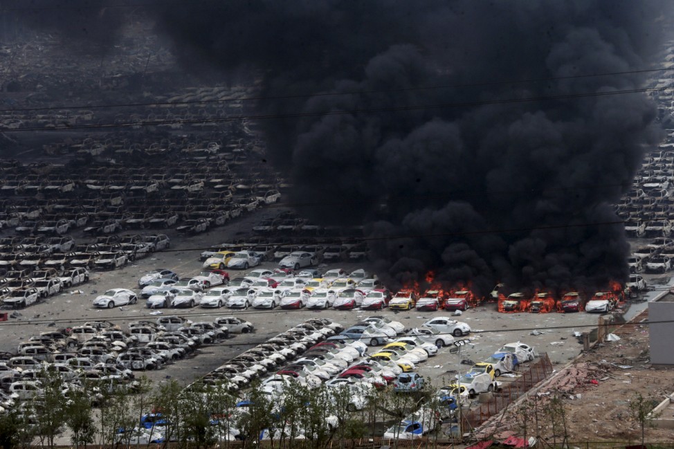 Smoke rises as damaged vehicles are seen burning near the site of the Wednesday night's explosions, at Binhai new district in Tianjin