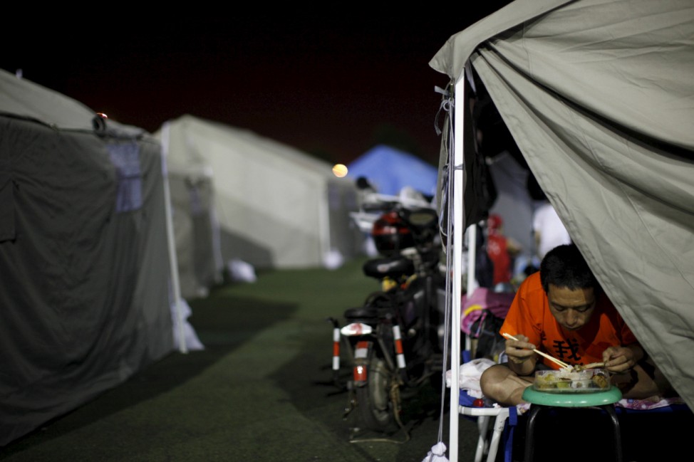 A man eats in a tent set up at a temporary shelter for people affected by Wednesday night's explosions, on the playground of a primary school at Binhai new district in Tianjin
