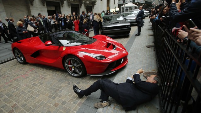 A man tries to take a picture of a Ferrari LaFerrari sports car parked at the entrance of the New York Stock Exchange in New York